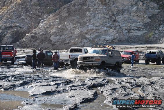 Gray 1996 Ford Bronco driving through mud with water splashing