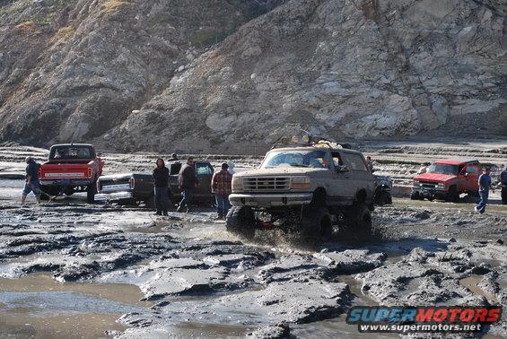 1996 Ford Bronco navigating a muddy off-road course with other trucks