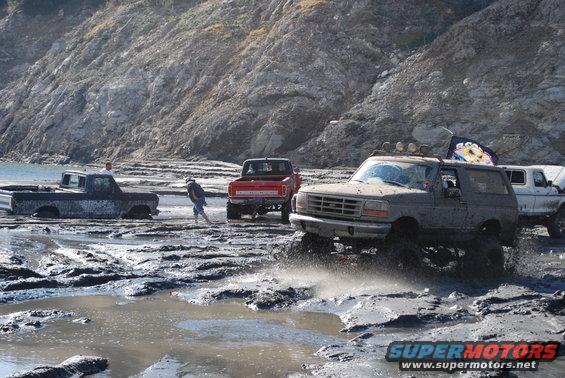 Gray 1996 Ford Bronco splashing through mud with other trucks nearby