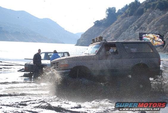 Dark SUV splashing through mud with another vehicle behind it
