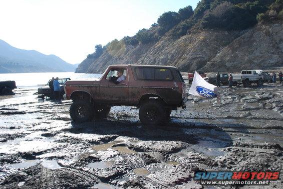Old Ford Bronco driving through mud with a Ford flag attached