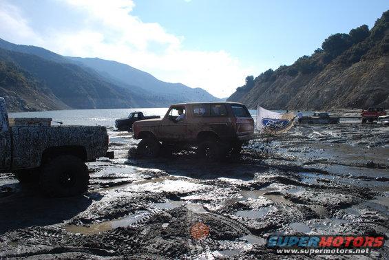 Brown Ford Bronco stuck in mud with a Ford flag behind it