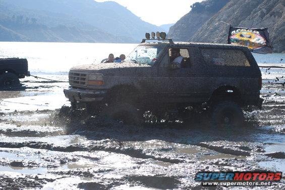 1996 Ford Bronco stuck in mud with people inside, another vehicle is visible being towed
