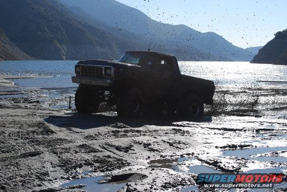 Lifted pickup truck driving through mud near a lake. Looks like a 1979 Ford F-Series