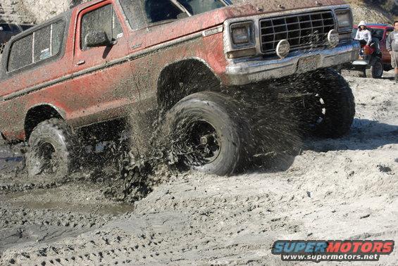 Red Ford Bronco splashing mud, front 3/4 view, lifted suspension, off-road tires
