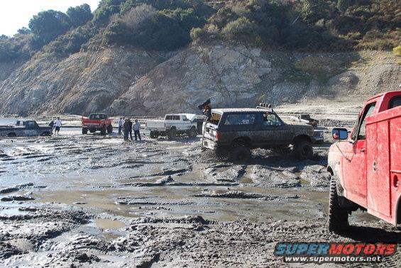 Muddy 1996 Ford Bronco in a muddy field with other trucks