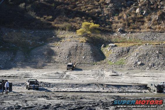 Dark SUV driving up muddy embankment with other vehicles nearby