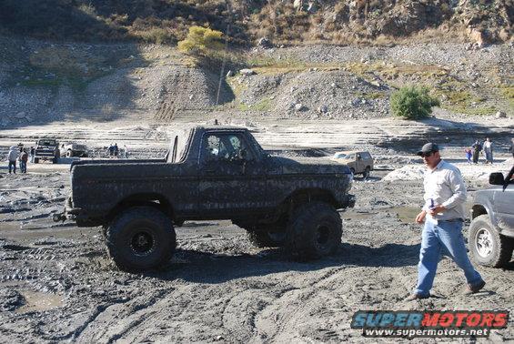 Mud-covered Ford Bronco with large tires, side view, off-road