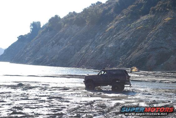 1996 Ford Bronco driving through a muddy, watery area with a rocky hill in the background