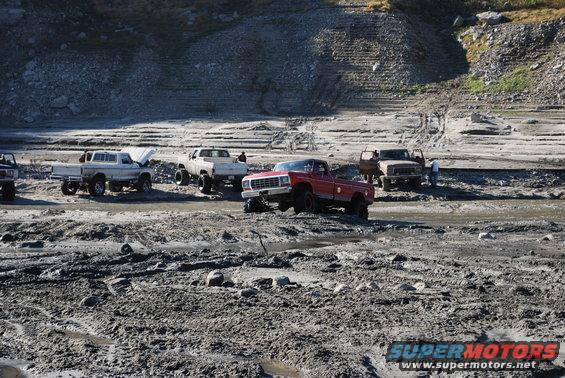Red pickup truck with lifted suspension in mud, other trucks visible in background