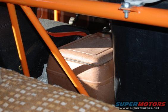 Interior shot of a vehicle showing a brown cooler behind orange roll cage bars and patterned seat fabric