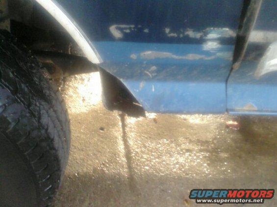 blue vehicle side panel, tire, and muddy ground. Supermotors.net logo in corner