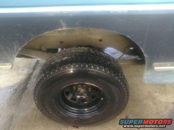 Rear wheel well and tire of a vehicle. Some rust is visible around the wheel opening