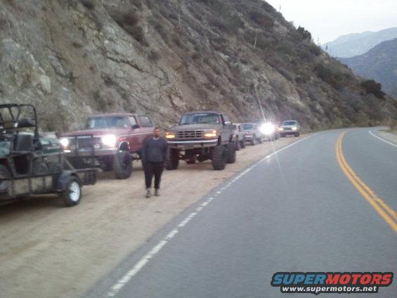 Lifted 1980s Ford F-series truck with large tires parked on a dirt shoulder next to a road