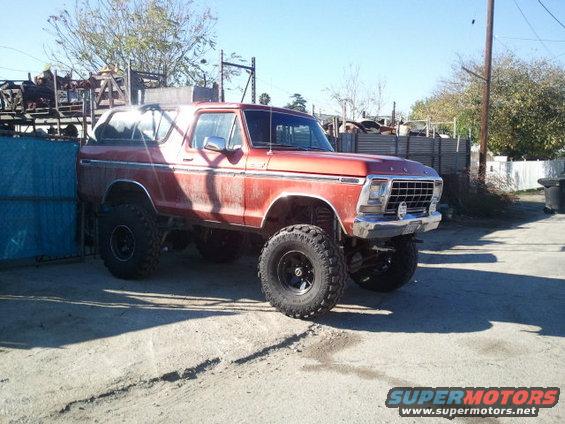 Red 1979 Ford Bronco with lifted suspension and large tires, viewed from the front three-quarter angle