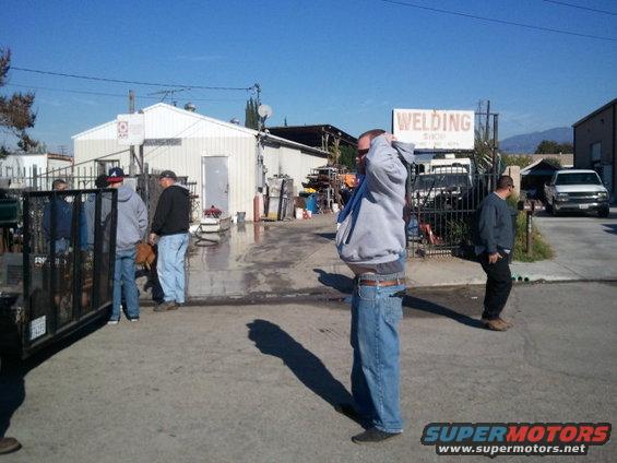 People gathered outside a welding shop with a white truck and a trailer