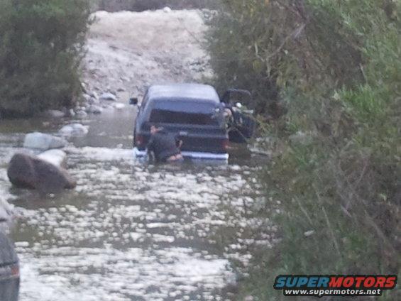 Black 1978 Ford Bronco partially submerged in a rocky stream with its rear facing the camera