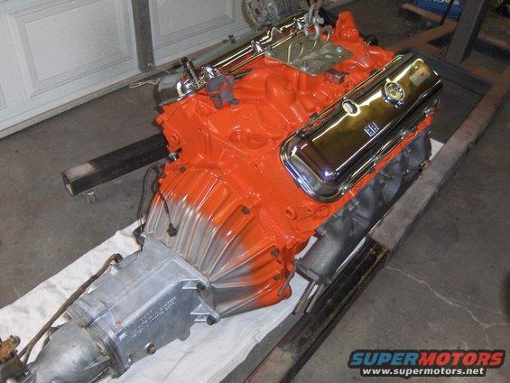 Orange V8 engine with chrome valve covers and transmission attached, resting on a white cloth