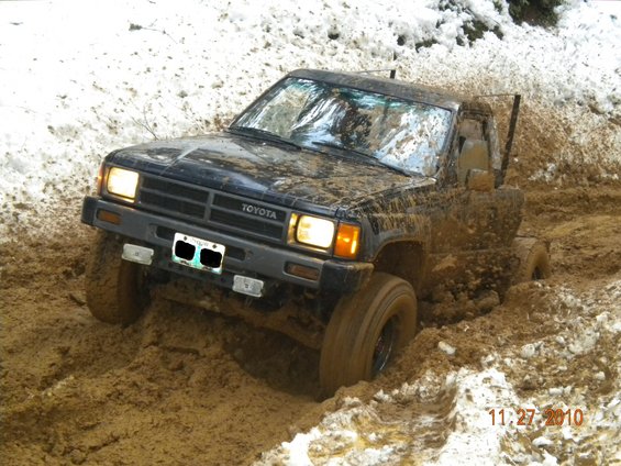 Mud-covered black Toyota pickup truck stuck in mud with snow on the ground