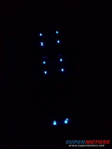 Glowing blue car door lock and window controls at night