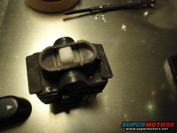 Car window switch assembly with a separate button showing a triangle pointing left. A screwdriver is in the background