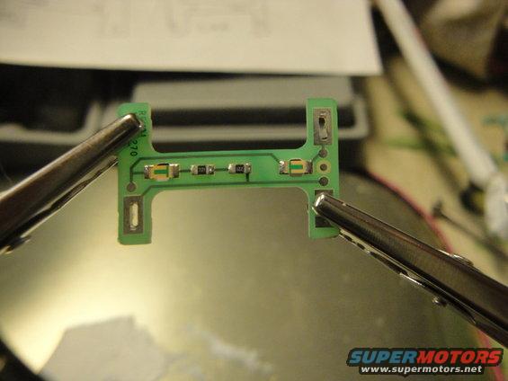 Circuit board held by alligator clips, with small electronic components. Text 'R2M 270' visible