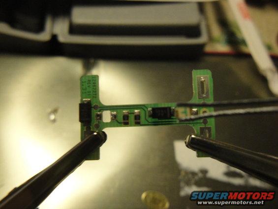 Circuit board held by tweezers, with text '12892212 REV 01 1.31' visible