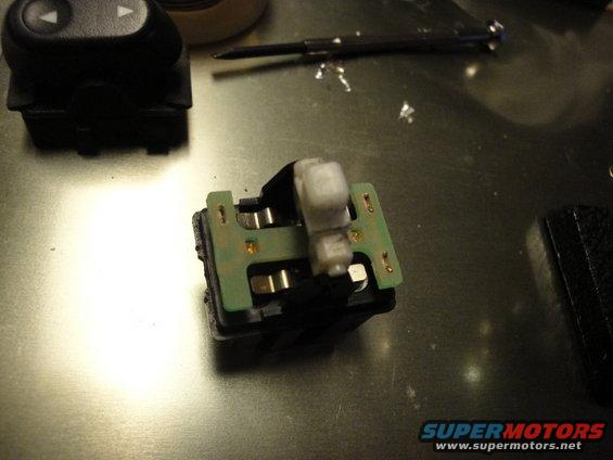 Car window switch assembly with green circuit board and white plastic actuator on a metallic surface