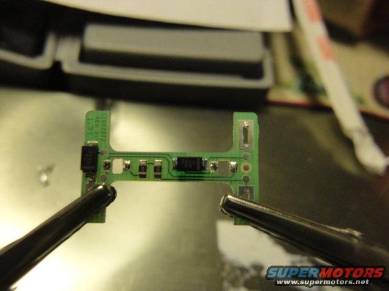 Circuit board held by tweezers, with small electronic components soldered on