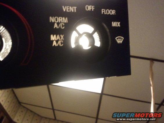 Black climate control panel with glowing knobs and text labels like VENT, NORM A/C, MAX A/C, OFF, FLOOR, MIX