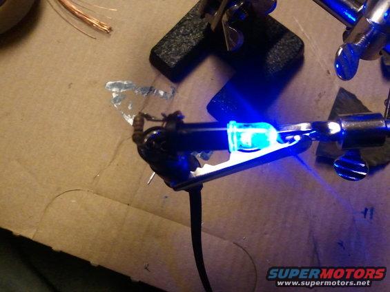 Soldering iron holding a blue LED light with wires and a circuit board