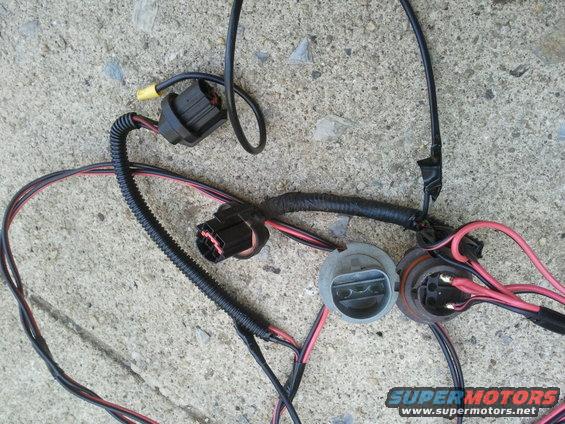 Automotive headlight wiring harness with two connectors and two bulb sockets, lying on concrete