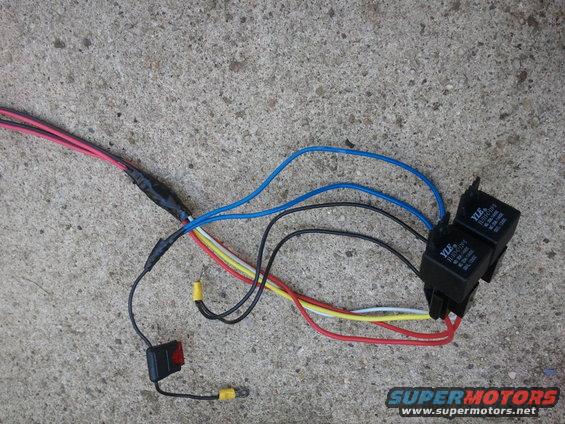 Automotive wiring harness with two black relays labeled YLE, a red-lit switch, and multi-colored wires on a concrete surface