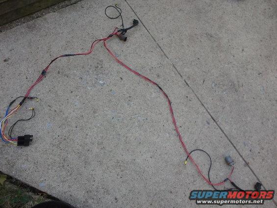 Automotive wiring harness with red and black wires, connectors, and a black plastic housing, laid out on concrete
