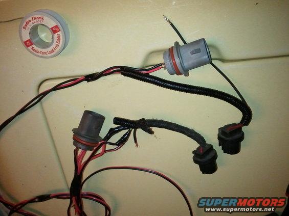 Headlight wiring harness with two grey connectors and two black connectors, next to a roll of solder
