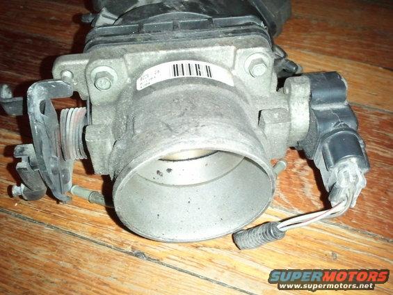 Close-up of a throttle body with a label that has a barcode and some text. Wires are connected to the side