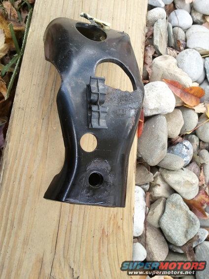 Black metal bracket with plastic clips, resting on wood and rocks