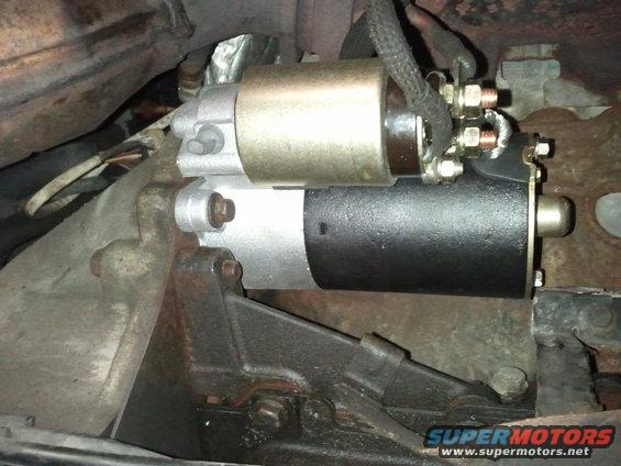 Close-up of a vehicle's starter motor, showing electrical connections and mounting bracket