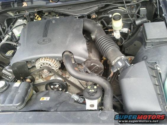 Engine bay of a 2003 Ford Crown Victoria, showing the engine cover, alternator, and air intake system