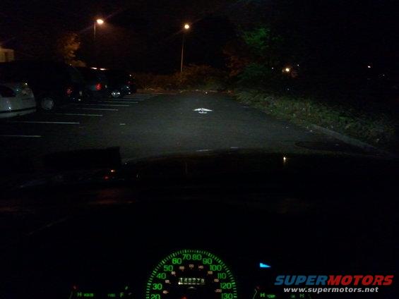 Car dashboard with illuminated speedometer and parking lot at night
