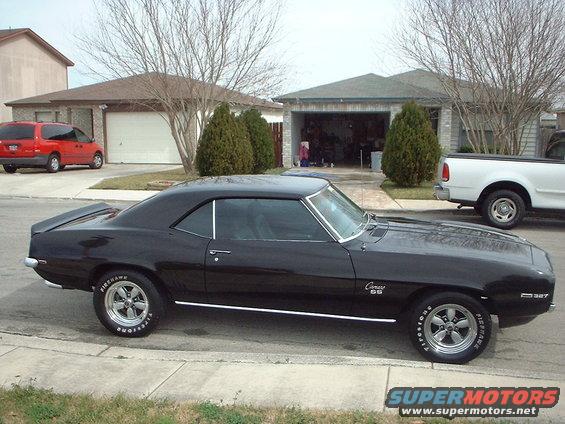 Black 1969 Chevrolet Camaro SS parked on street, white pickup truck and red minivan in background