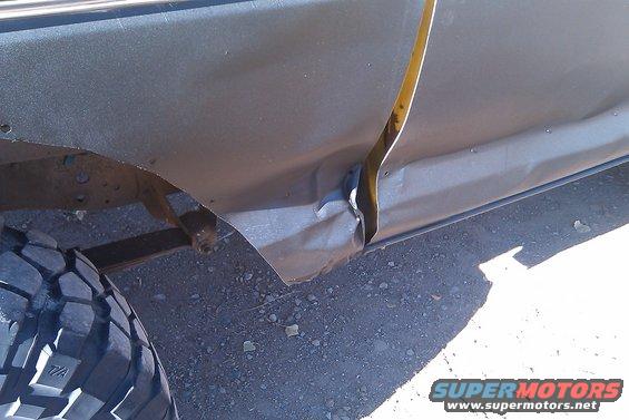 Side of a vehicle with significant damage to the lower body panel and door jamb. Tire visible