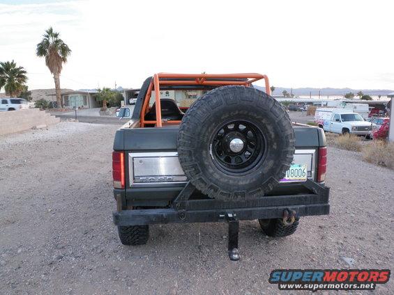 Rear view of a Ford Bronco with an external spare tire mount and orange roll cage. License plate reads 08006
