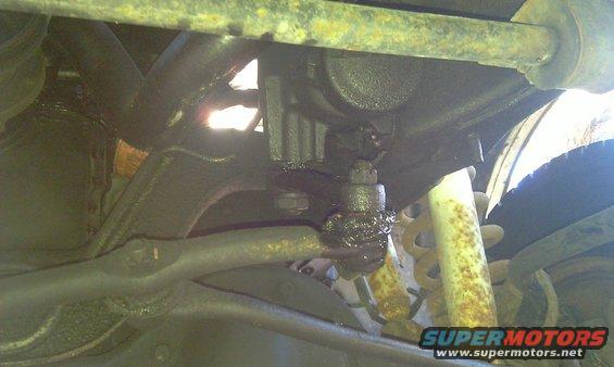 Underside of a vehicle showing greasy suspension parts and a rusty shock absorber