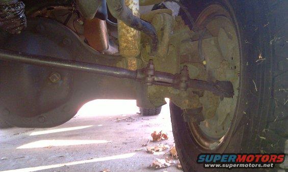 Close-up of a vehicle's rear axle, differential, and suspension components. Shows the steering linkage and part of the tire