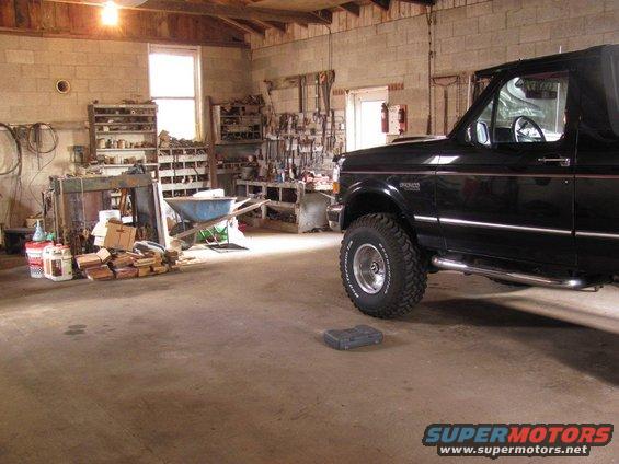 Black 1995 Ford Bronco parked in a cluttered garage with tools and a wheelbarrow