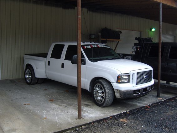 White dually pickup truck with chrome wheels parked under a cover, front 3/4 view