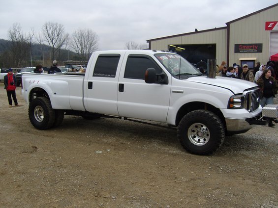 White Ford F-350 Super Duty dually pickup truck with large exhaust stack, lifted suspension, and aftermarket wheels