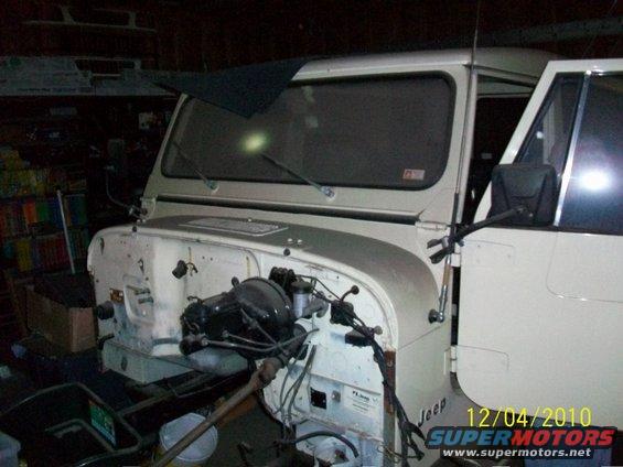White Jeep CJ-8 Scrambler with hood removed, showing engine bay and open driver's door