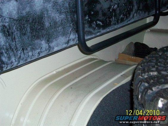 Inside of a Jeep, showing the wheel well and cargo area floor. A spare tire is visible on the right